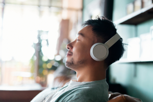 Young Asian man with eyes closed, enjoying music over headphones while relaxing on the sofa at home